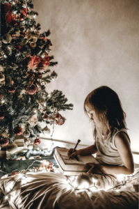 Child writing a family prayer at Christmastime, fitting Jesus into the holidays.