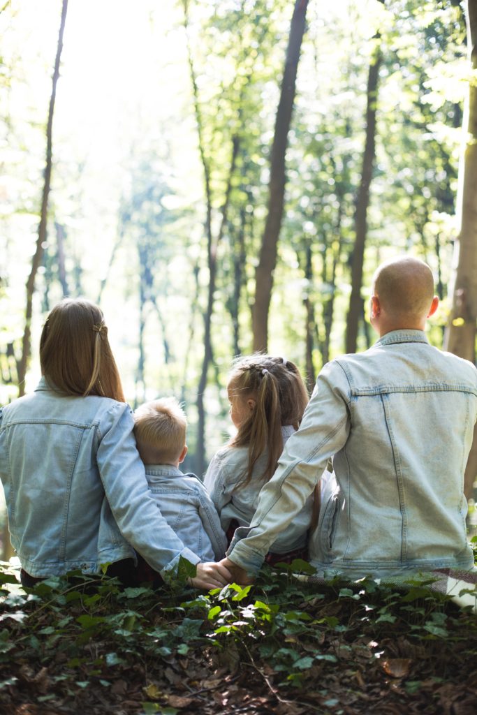 Photo of husband and wife parenting their two children between them in the woods.
