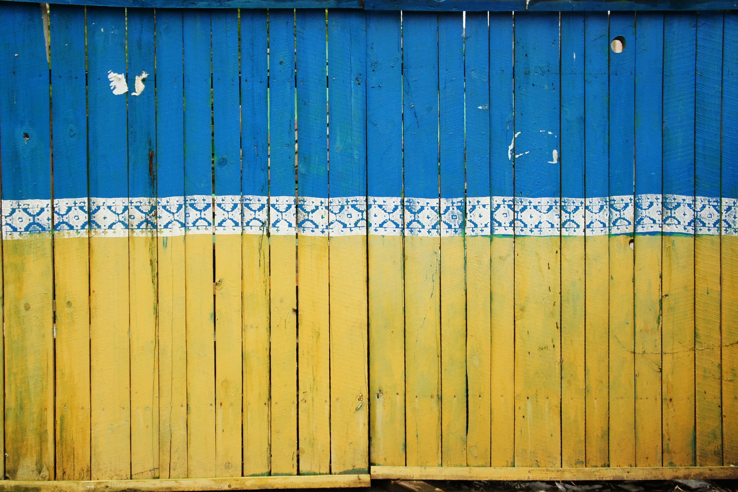 A fence painted in the colors of Ukraine symbolizing a common childhood play area of a fence, with the Ukrainian colors present as well.